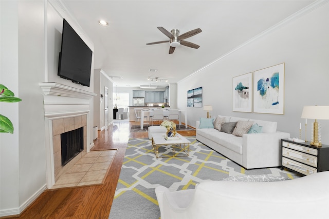 living room with hardwood / wood-style floors, crown molding, a tiled fireplace, and ceiling fan