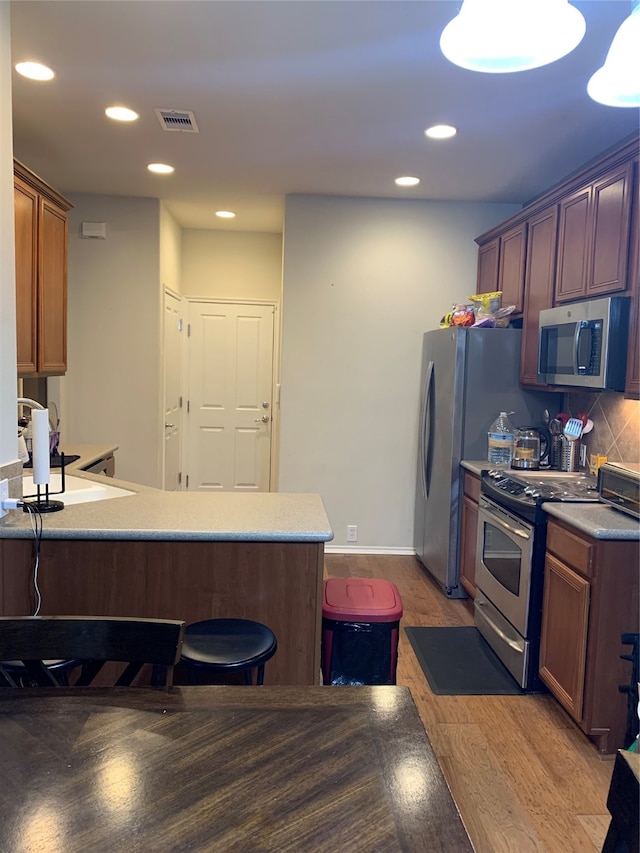 kitchen featuring hardwood / wood-style floors, tasteful backsplash, kitchen peninsula, pendant lighting, and appliances with stainless steel finishes