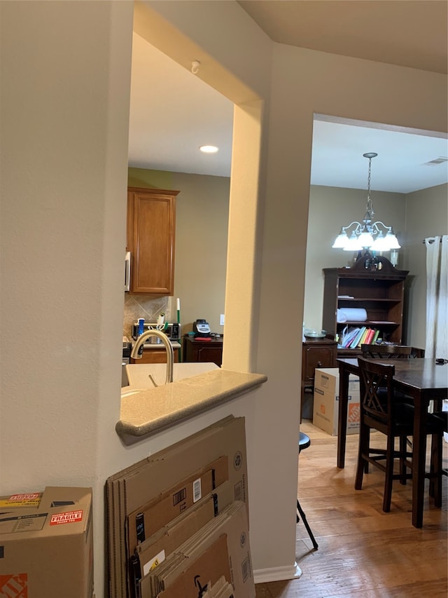 kitchen with decorative light fixtures, an inviting chandelier, a kitchen bar, tasteful backsplash, and light hardwood / wood-style flooring