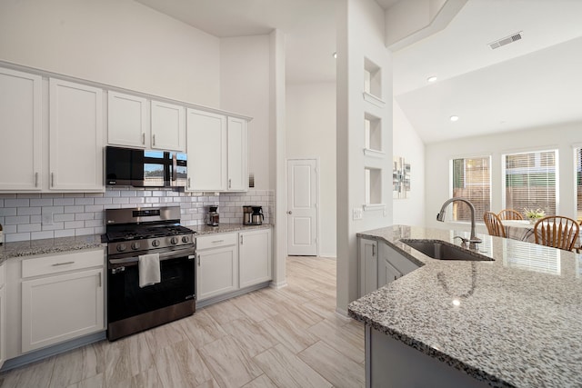 kitchen with high vaulted ceiling, light stone counters, white cabinets, sink, and stainless steel gas range oven