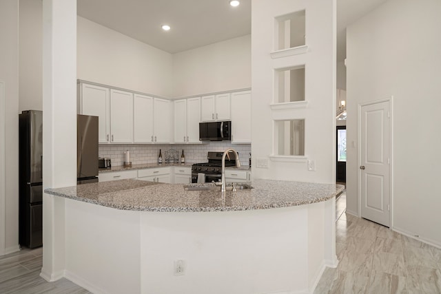 kitchen featuring a high ceiling, light stone counters, stainless steel appliances, and white cabinets