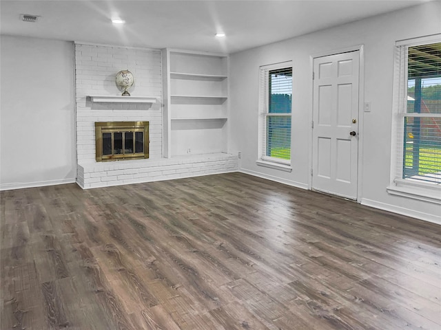 unfurnished living room with dark hardwood / wood-style flooring, a brick fireplace, and built in shelves