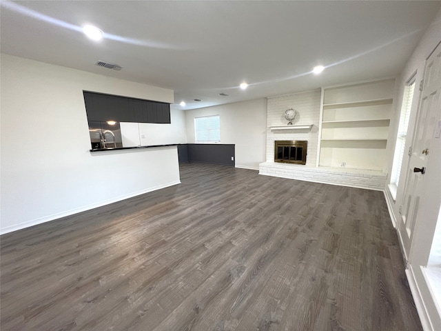 unfurnished living room featuring sink, dark hardwood / wood-style flooring, a fireplace, and built in shelves