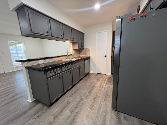 kitchen featuring decorative backsplash, sink, light wood-type flooring, gray cabinets, and appliances with stainless steel finishes