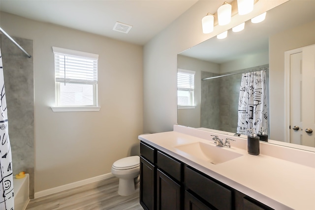 full bathroom featuring wood-type flooring, a healthy amount of sunlight, vanity, and toilet