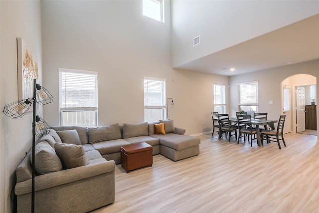 living room with a towering ceiling, light hardwood / wood-style flooring, and plenty of natural light