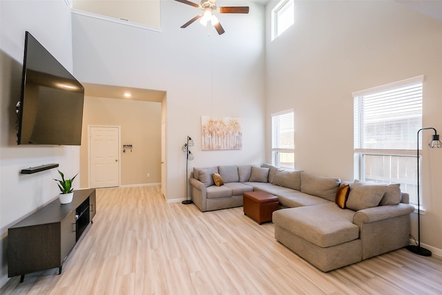 living room featuring ceiling fan, plenty of natural light, a towering ceiling, and light hardwood / wood-style floors