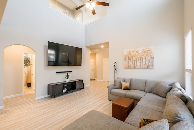 living room with a high ceiling, light wood-type flooring, and ceiling fan