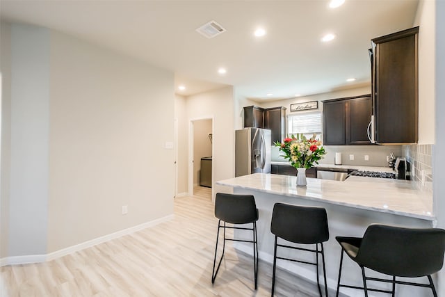 kitchen with stainless steel appliances, light wood-type flooring, kitchen peninsula, and decorative backsplash