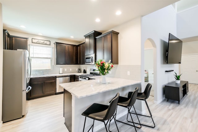 kitchen featuring light stone counters, kitchen peninsula, appliances with stainless steel finishes, a breakfast bar, and light hardwood / wood-style floors