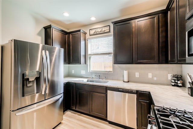 kitchen with light stone counters, sink, tasteful backsplash, stainless steel appliances, and light hardwood / wood-style floors