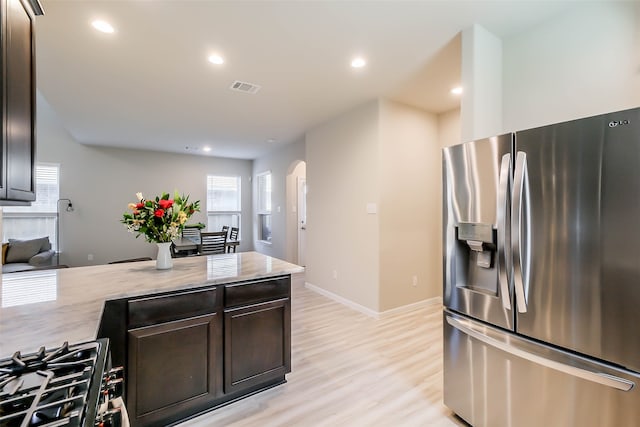 kitchen featuring light stone countertops, appliances with stainless steel finishes, light wood-type flooring, and dark brown cabinets