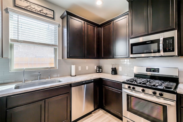 kitchen featuring dark brown cabinetry, light stone counters, sink, appliances with stainless steel finishes, and decorative backsplash