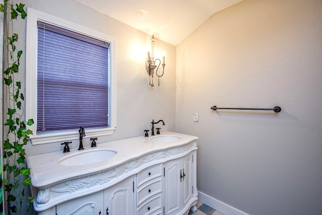 full bath with double vanity, baseboards, vaulted ceiling, and a sink