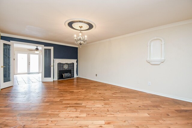 unfurnished living room featuring crown molding, a tiled fireplace, french doors, and light hardwood / wood-style floors