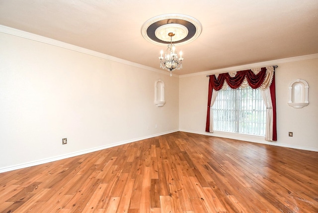 spare room with a chandelier, crown molding, wood finished floors, and baseboards