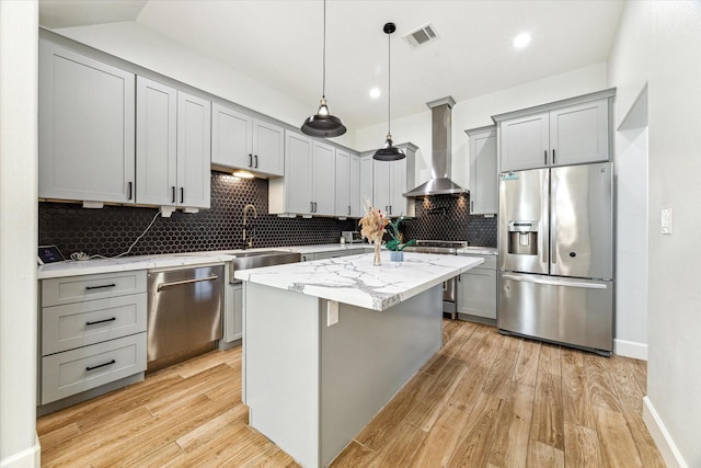 kitchen featuring light wood-type flooring, tasteful backsplash, stainless steel appliances, wall chimney range hood, and decorative light fixtures