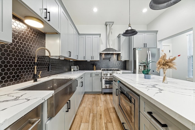 kitchen with backsplash, wall chimney exhaust hood, stainless steel appliances, decorative light fixtures, and light hardwood / wood-style flooring