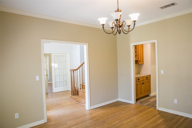 empty room featuring wood-type flooring, a notable chandelier, and ornamental molding