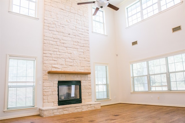 unfurnished living room featuring a towering ceiling, hardwood / wood-style flooring, and a stone fireplace