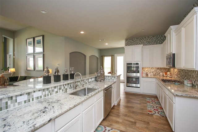 kitchen featuring appliances with stainless steel finishes, sink, white cabinets, light stone counters, and light hardwood / wood-style flooring