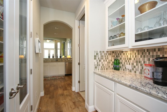 bar featuring white cabinetry, dishwasher, wood-type flooring, and light stone counters