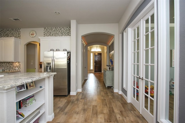 kitchen featuring tasteful backsplash, hardwood / wood-style floors, white cabinetry, light stone counters, and stainless steel refrigerator with ice dispenser