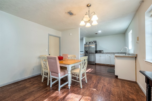 dining space featuring dark wood-type flooring, a textured ceiling, sink, and a chandelier