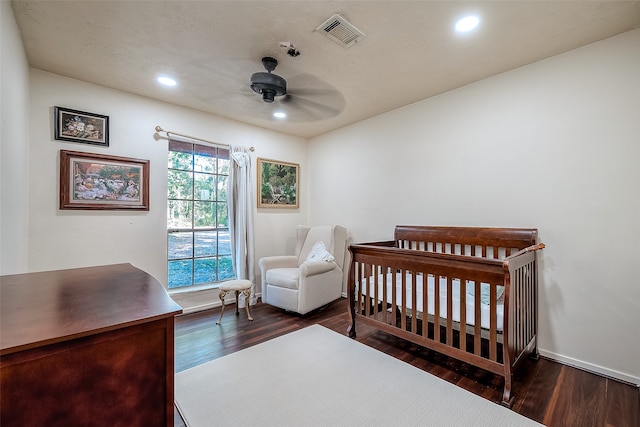 bedroom featuring ceiling fan, dark hardwood / wood-style flooring, and a nursery area