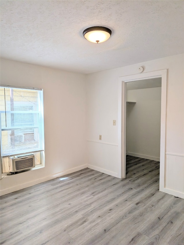 empty room with light hardwood / wood-style flooring, cooling unit, and a textured ceiling