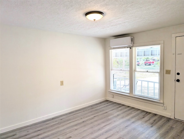 empty room featuring a textured ceiling, a wall mounted air conditioner, and light hardwood / wood-style floors