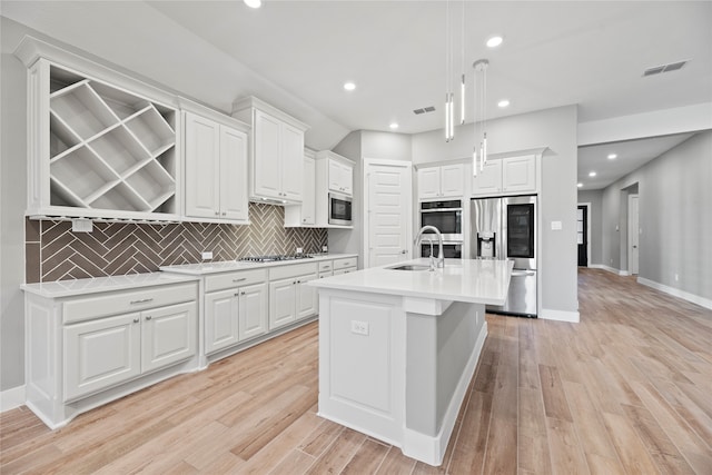 kitchen featuring a kitchen island with sink, hanging light fixtures, white cabinets, appliances with stainless steel finishes, and light hardwood / wood-style floors