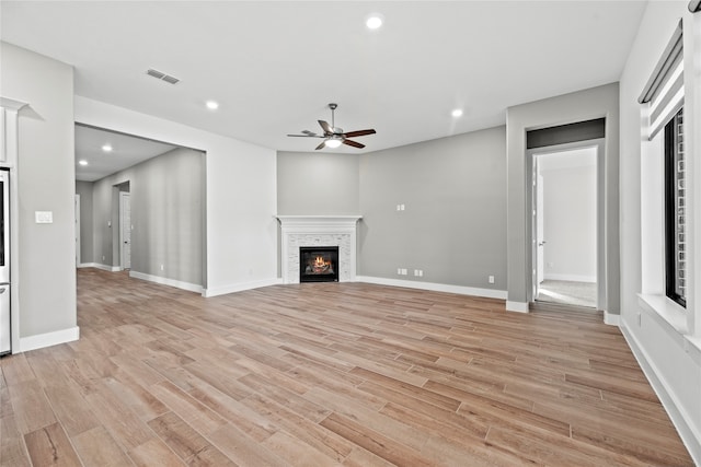 unfurnished living room with light hardwood / wood-style floors, a stone fireplace, and ceiling fan