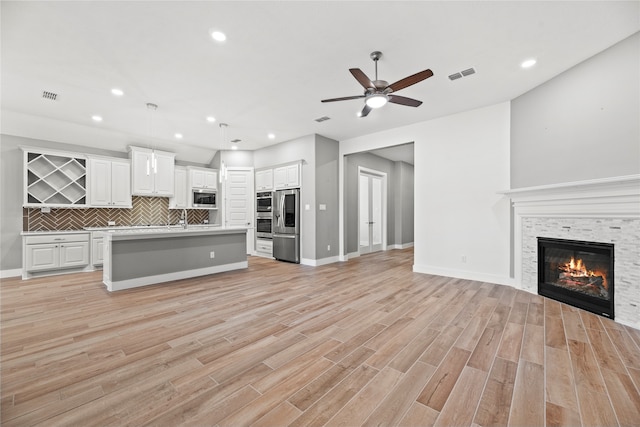 unfurnished living room with light hardwood / wood-style floors, a stone fireplace, sink, and ceiling fan