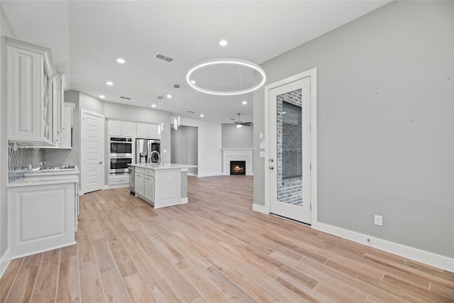 kitchen with light hardwood / wood-style floors, appliances with stainless steel finishes, decorative light fixtures, and a center island with sink