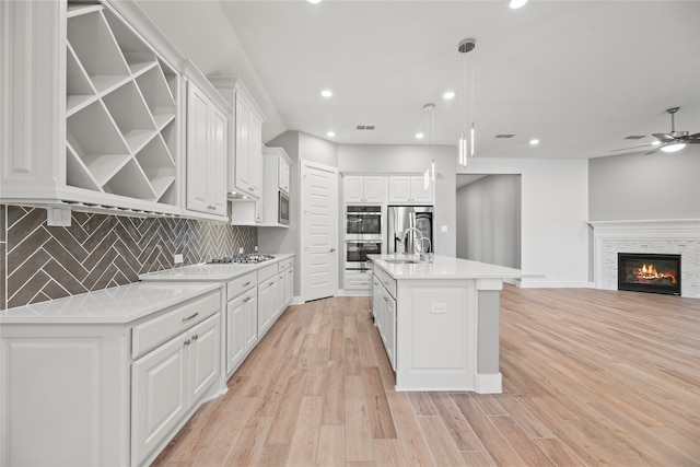 kitchen featuring white cabinets, light wood-type flooring, pendant lighting, and an island with sink