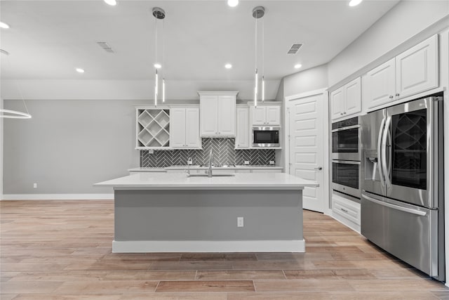 kitchen featuring light hardwood / wood-style floors, a kitchen island with sink, stainless steel appliances, and hanging light fixtures