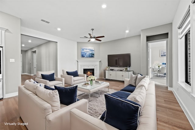 living room with light hardwood / wood-style floors, a stone fireplace, and ceiling fan