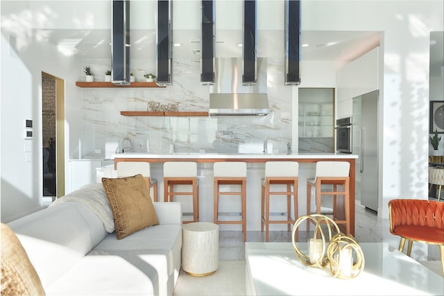 kitchen featuring wall chimney range hood, sink, white cabinetry, tasteful backsplash, and oven