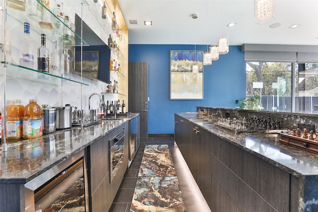 bar with sink, dark stone countertops, dark brown cabinets, wine cooler, and decorative light fixtures