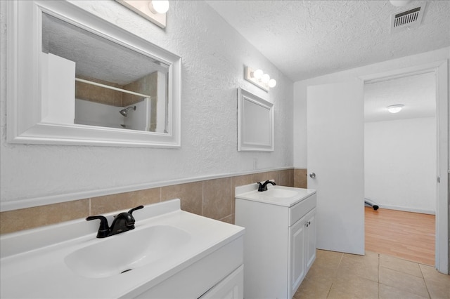 bathroom featuring tile patterned flooring, vanity, tile walls, a textured ceiling, and walk in shower