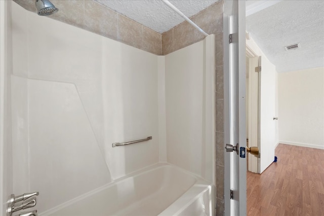 bathroom featuring hardwood / wood-style floors, washtub / shower combination, and a textured ceiling