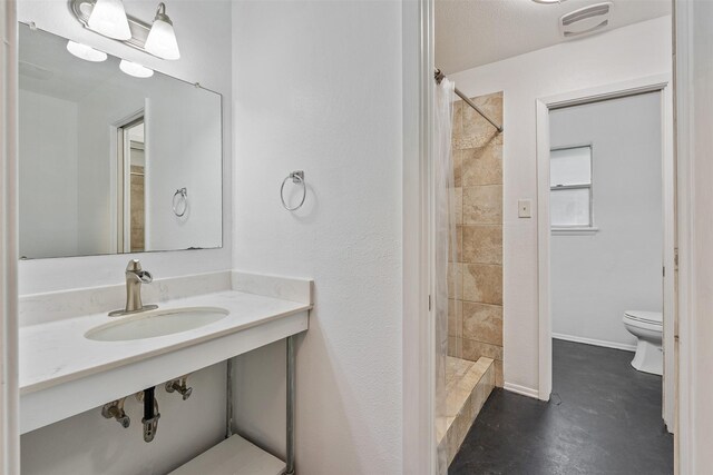 bathroom with a tile shower, sink, a textured ceiling, concrete flooring, and toilet