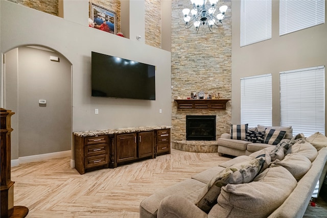 living room featuring a notable chandelier, a stone fireplace, a high ceiling, and light parquet floors