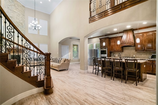 interior space featuring a breakfast bar, hanging light fixtures, a high ceiling, custom exhaust hood, and light hardwood / wood-style flooring