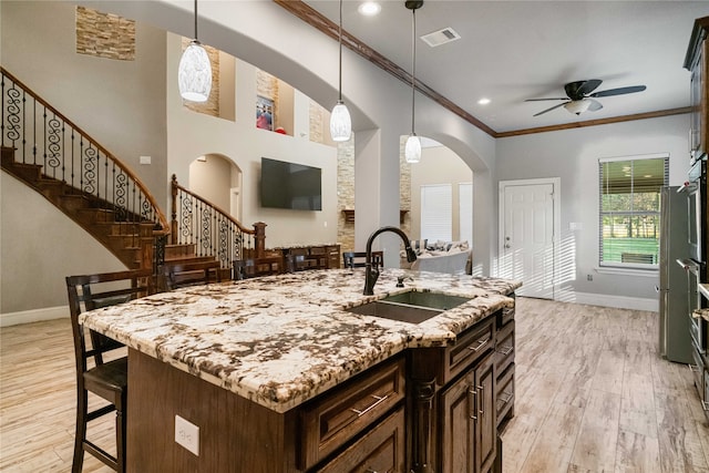 kitchen featuring ceiling fan, a kitchen island with sink, light wood-type flooring, ornamental molding, and decorative light fixtures