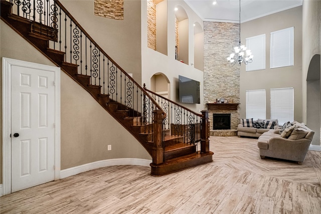 stairway with hardwood / wood-style floors, an inviting chandelier, a stone fireplace, ornamental molding, and a towering ceiling