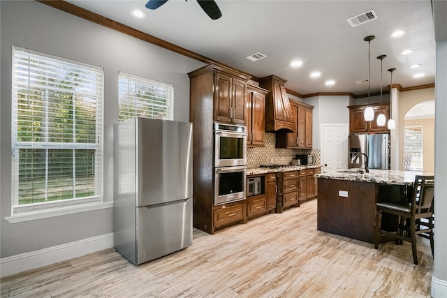 kitchen featuring an island with sink, stainless steel appliances, a breakfast bar, light stone countertops, and light hardwood / wood-style floors