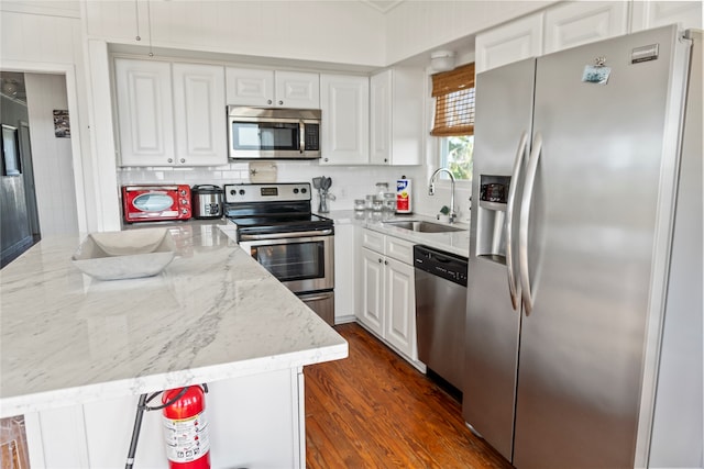 kitchen featuring white cabinets, appliances with stainless steel finishes, light stone countertops, sink, and a center island