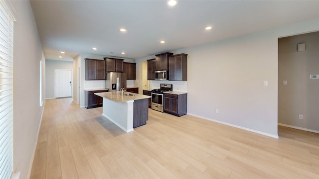 kitchen featuring an island with sink, sink, light stone countertops, appliances with stainless steel finishes, and light hardwood / wood-style floors